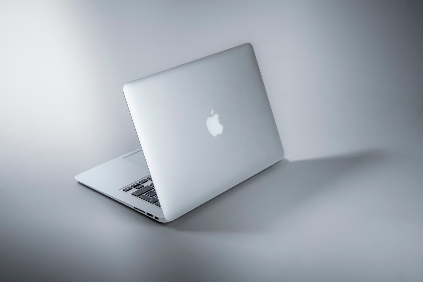 MacBook prateado entreaberto sobre fundo claro, visto de trás