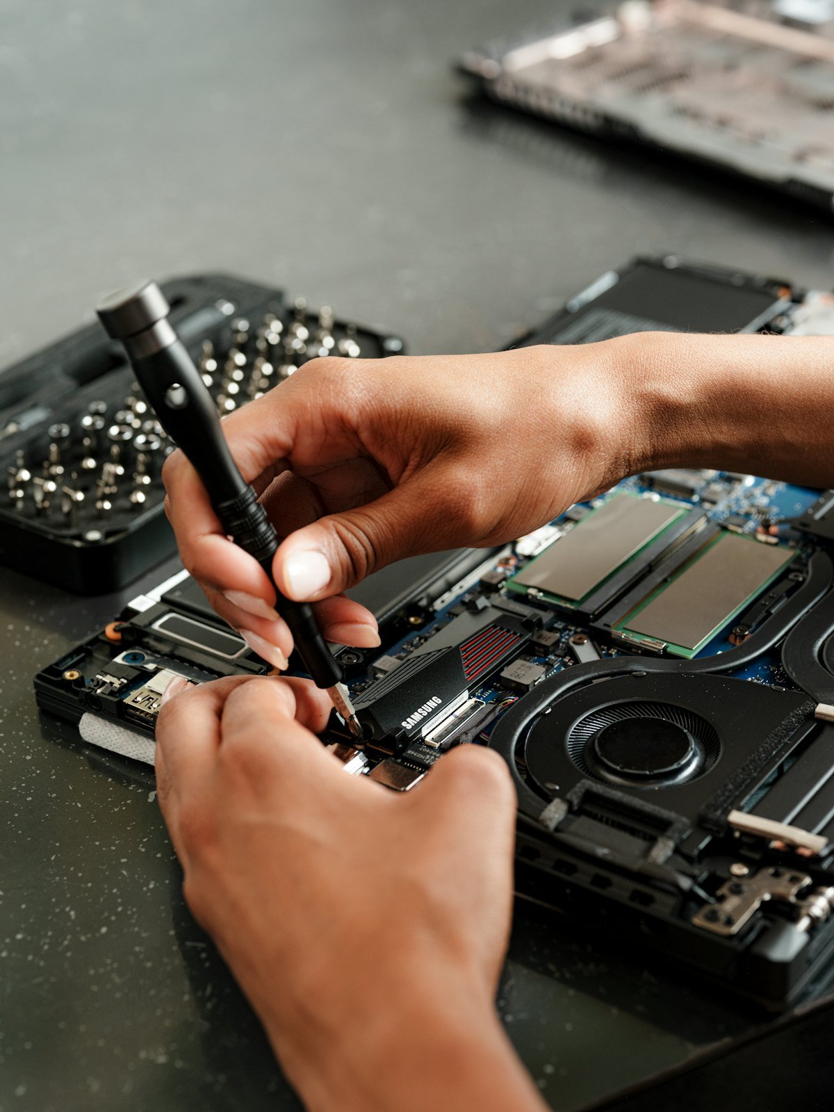 Mãos usando chave de precisão sobre a placa lógica de um notebook aberto, com componentes e dissipadores à mostra